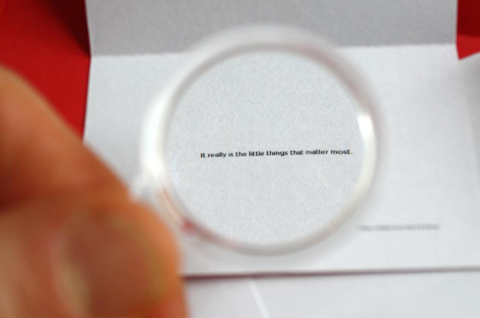 A close-up through the magnifying glass reveals the line of text: "It really is the little things that matter most."