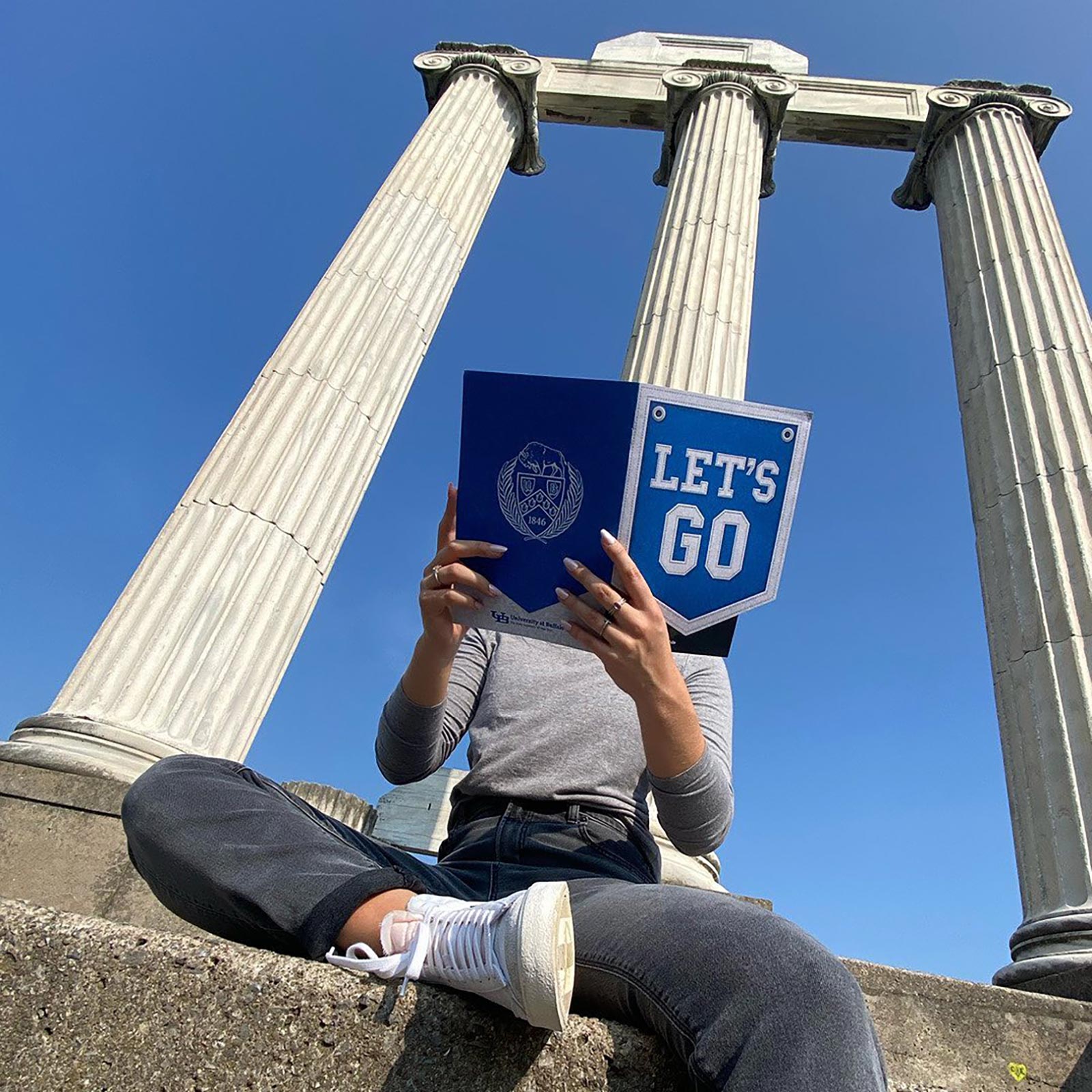 UB Prospect Mailer held by a student sitting at the Baird Point columns.
